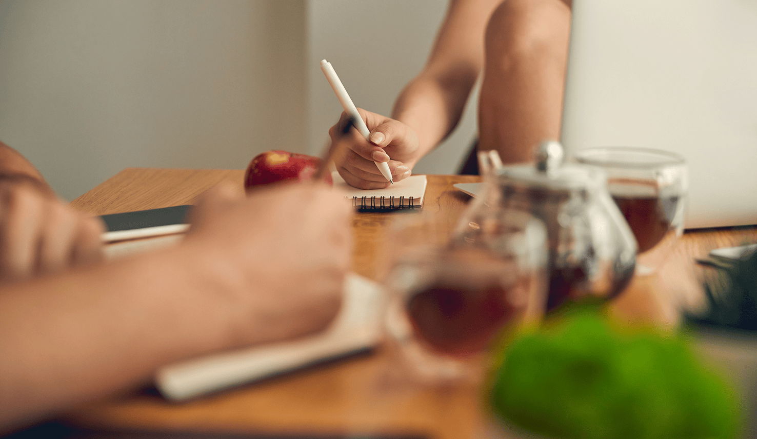 Close-up of a person taking notes in a small notebook at a table with tea and fruit and cup of tea nearby.