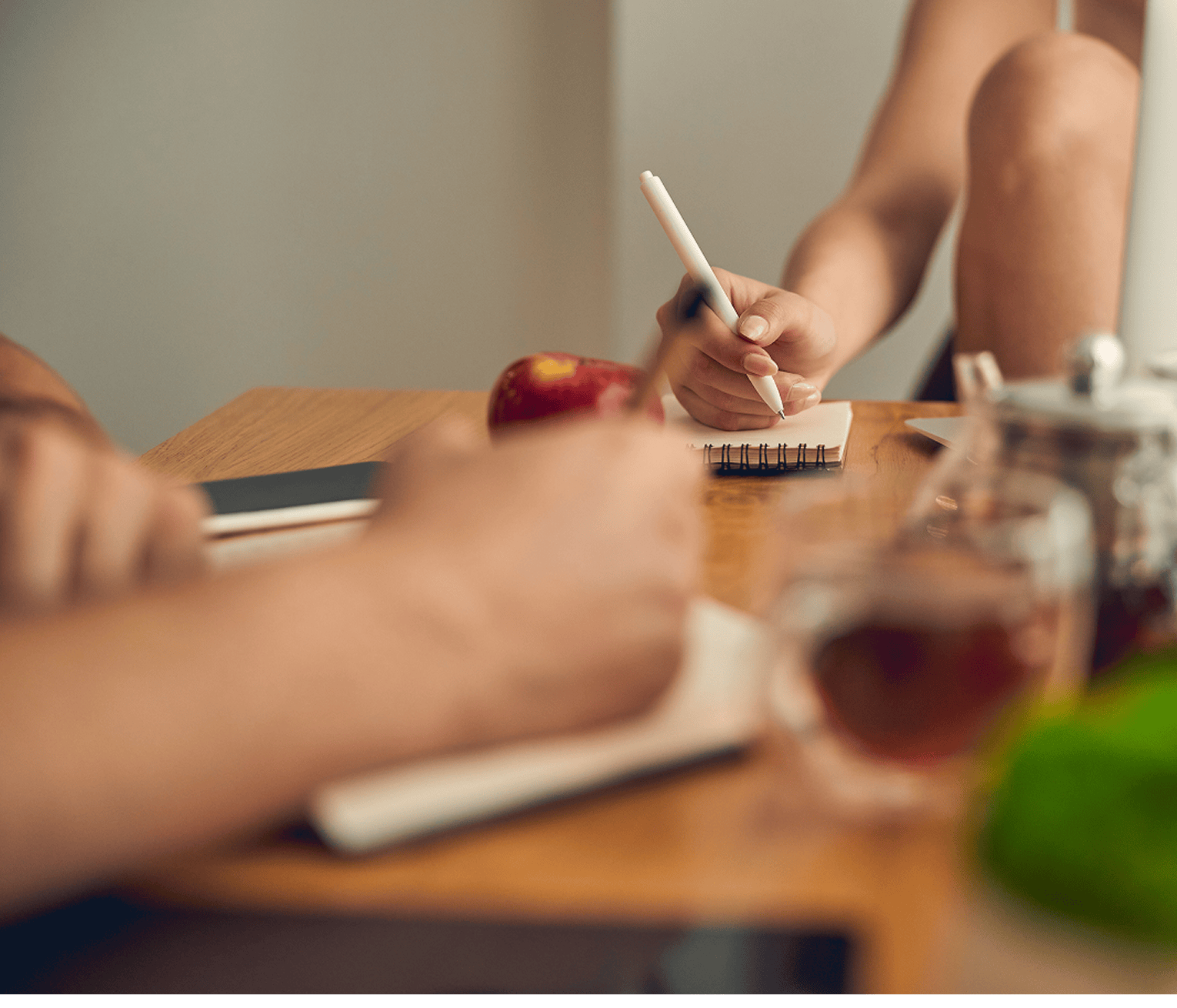 Close-up of a person taking notes in a small notebook at a table with tea and fruit and cup of tea nearby.