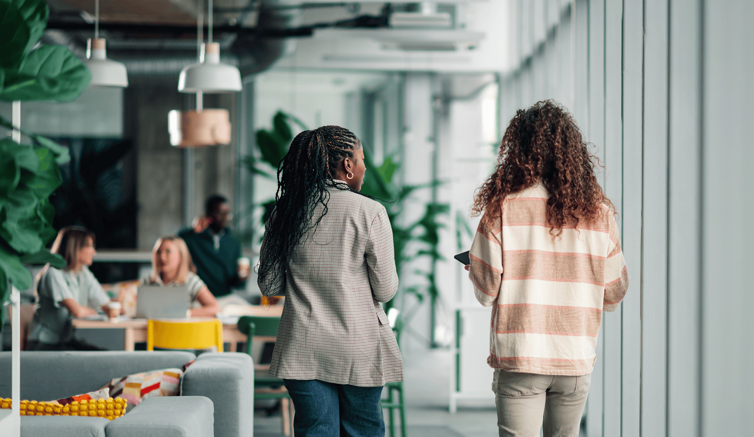 Two colleagues walking through a modern office space while team members work and collaborate in the background