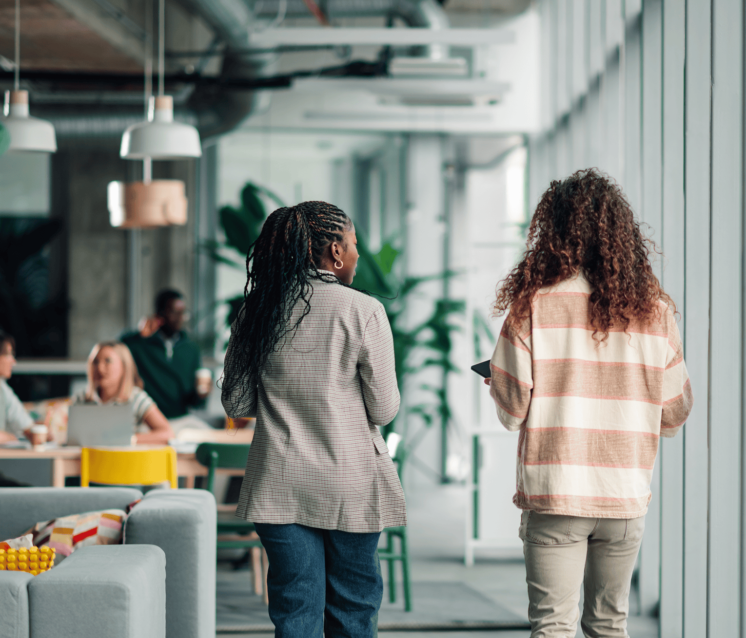 Two colleagues walking through a modern office space while team members work and collaborate in the background
