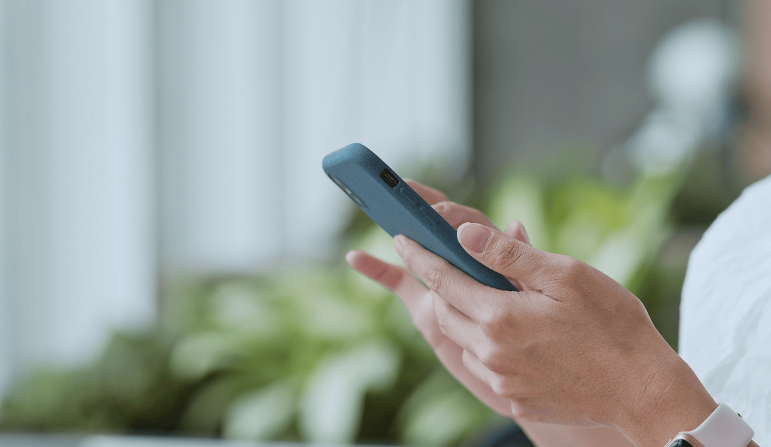 Close-up of hands holding a smartphone in a modern office setting.