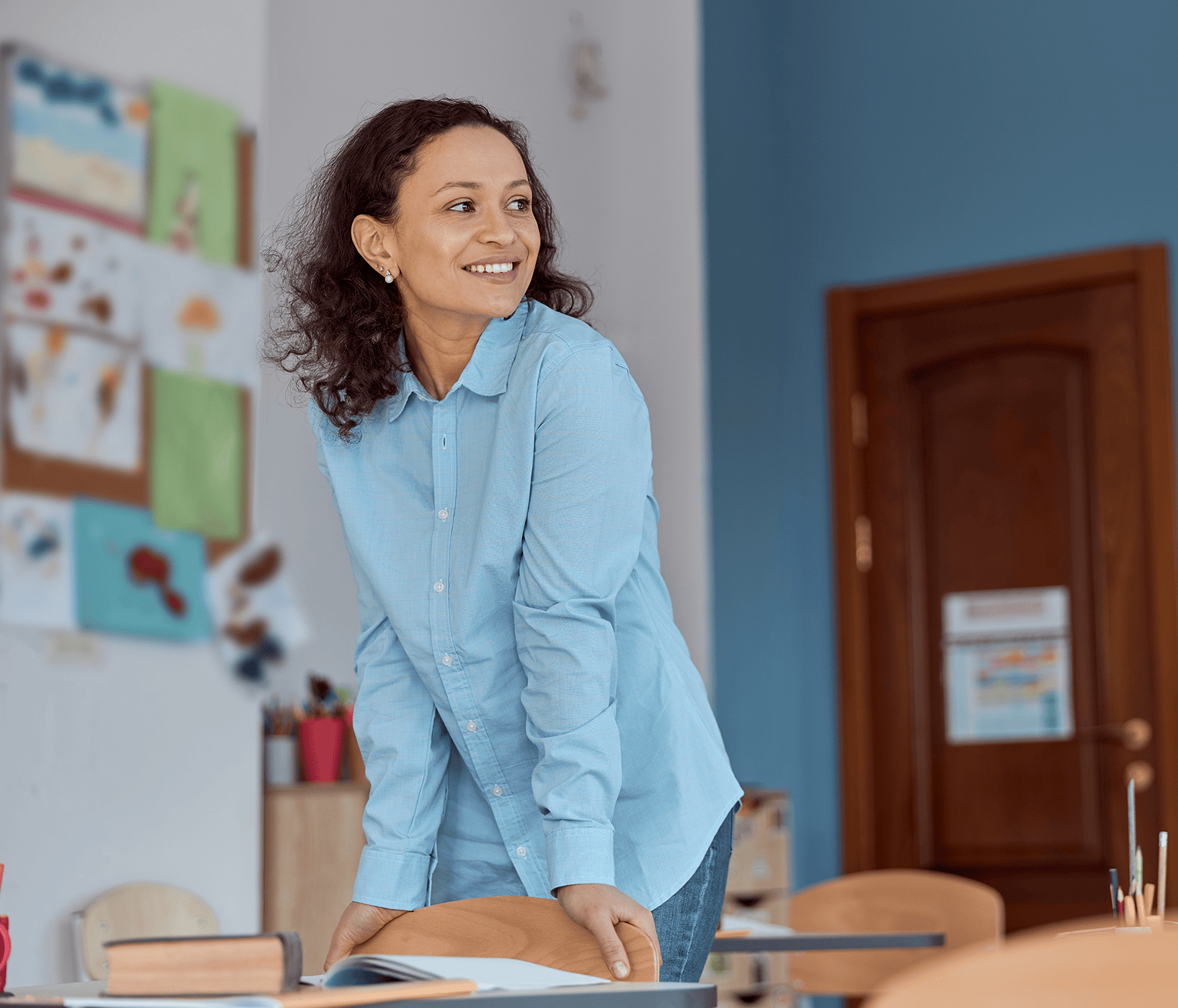 A school staff member wearing a light blue shirt stands in an empty classroom, preparing for the school day.